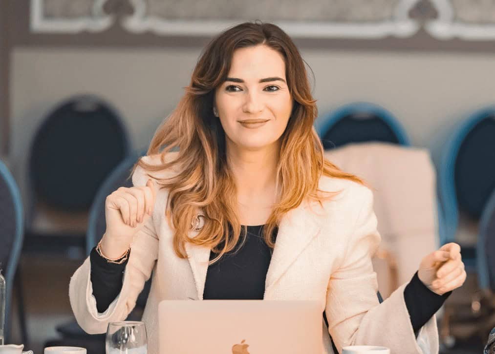 Femeie zâmbitoare la o întâlnire, laptop pe masă.